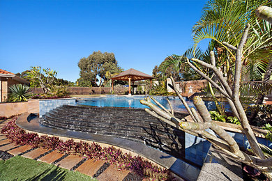 This is an example of an expansive mediterranean backyard custom-shaped infinity pool in Perth with a water feature and decking.