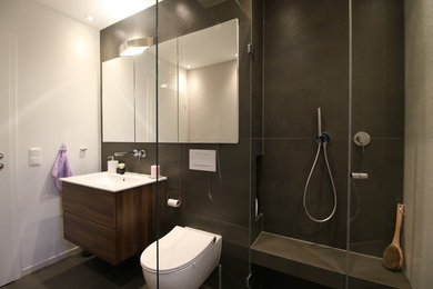 This is an example of a mid-sized contemporary 3/4 bathroom in Cologne with flat-panel cabinets, dark wood cabinets, a curbless shower, a two-piece toilet, gray tile, purple walls and grey floor.