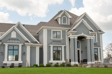 Photo of an expansive transitional two-storey stucco grey house exterior in Milwaukee with a gable roof and a shingle roof.