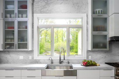 Minimalist light wood floor and gray floor kitchen photo in Philadelphia with a farmhouse sink, glass-front cabinets, white cabinets, marble countertops, gray backsplash, marble backsplash, stainless steel appliances, an island and gray countertops