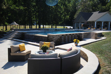This is an example of a large traditional backyard rectangular infinity pool in DC Metro with a hot tub and natural stone pavers.