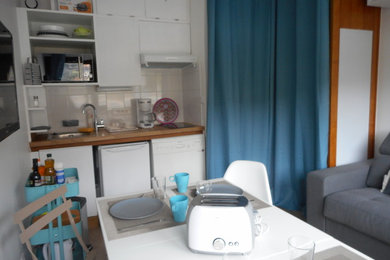 Inspiration pour une petite cuisine américaine linéaire minimaliste avec un évier 1 bac, des portes de placard blanches, un plan de travail en bois, une crédence blanche, une crédence en carreau de porcelaine, un électroménager en acier inoxydable et un sol en linoléum.