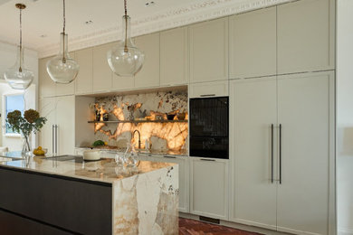 Large contemporary cream and black single-wall kitchen/diner in London with an integrated sink, shaker cabinets, beige cabinets, marble worktops, multi-coloured splashback, marble splashback, black appliances, dark hardwood flooring, an island, multicoloured worktops and feature lighting.