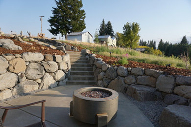 Expansive country sloped full sun xeriscape in Portland with a retaining wall and mulch.