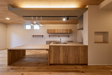 Imagen de cocina lineal abierta con suelo de contrachapado, una isla, papel pintado, puertas de armario de madera clara y encimera de madera