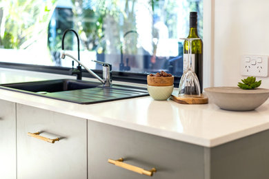 Small modern single-wall eat-in kitchen in Brisbane with a single-bowl sink, solid surface benchtops, window splashback, light hardwood floors, no island and white benchtop.