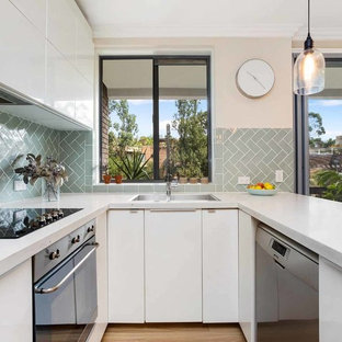 Design ideas for a mid-sized contemporary u-shaped kitchen pantry in Sydney with an undermount sink, flat-panel cabinets, white cabinets, marble benchtops, green splashback, cement tile splashback, stainless steel appliances, laminate floors, with island, beige floor and white benchtop.
