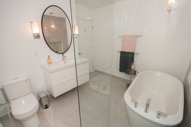 Example of a large trendy master gray tile and porcelain tile porcelain tile and gray floor bathroom design in Toronto with flat-panel cabinets, white cabinets, a one-piece toilet, white walls, an integrated sink, a hinged shower door and white countertops