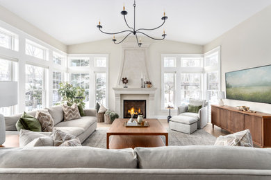 Inspiration for a large transitional open concept medium tone wood floor and brown floor living room remodel in Other with beige walls, a standard fireplace, a plaster fireplace and a wall-mounted tv