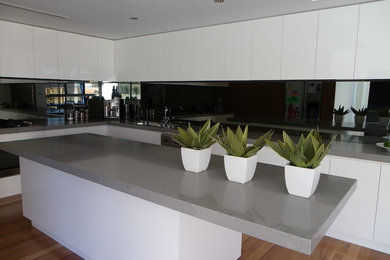 Photo of a large modern l-shaped kitchen pantry in Perth with an undermount sink, white cabinets, quartz benchtops, mirror splashback, light hardwood floors and with island.