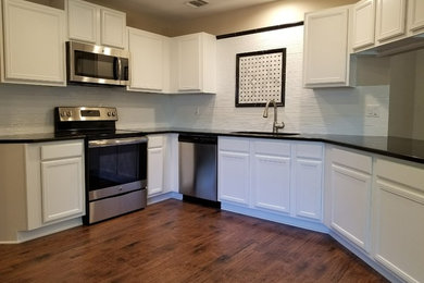 Eat-in kitchen - mid-sized traditional u-shaped dark wood floor and brown floor eat-in kitchen idea in Austin with an undermount sink, recessed-panel cabinets, white cabinets, quartz countertops, white backsplash, stainless steel appliances and no island