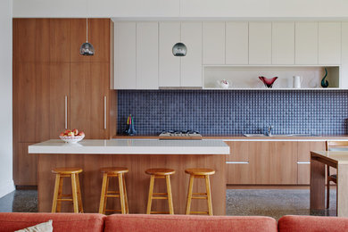 Photo of a large contemporary galley open plan kitchen in Melbourne with a drop-in sink, flat-panel cabinets, medium wood cabinets, blue splashback, with island, granite benchtops, ceramic splashback, stainless steel appliances, concrete floors and grey floor.