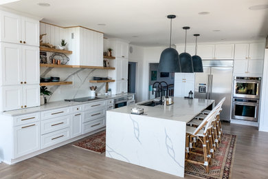 This is an example of a large scandinavian l-shaped eat-in kitchen in Louisville with a single-bowl sink, shaker cabinets, white cabinets, quartz benchtops, white splashback, engineered quartz splashback, stainless steel appliances, light hardwood floors, with island, brown floor and white benchtop.
