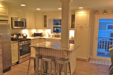 Eat-in kitchen - mid-sized coastal l-shaped medium tone wood floor eat-in kitchen idea in New York with a farmhouse sink, recessed-panel cabinets, white cabinets, marble countertops, white backsplash, stainless steel appliances and an island