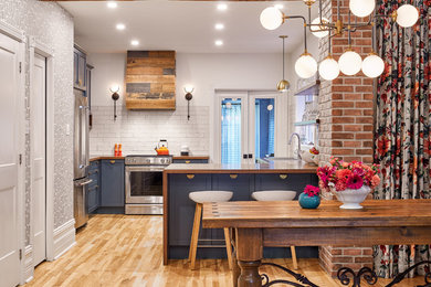 Example of a small transitional l-shaped medium tone wood floor and brown floor open concept kitchen design in Ottawa with a drop-in sink, recessed-panel cabinets, blue cabinets, wood countertops, white backsplash, ceramic backsplash, stainless steel appliances, a peninsula and brown countertops
