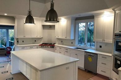 Photo of a mid-sized traditional u-shaped eat-in kitchen in New York with a drop-in sink, flat-panel cabinets, quartz benchtops, white splashback, marble splashback, stainless steel appliances, with island, brown floor, white benchtop, white cabinets and light hardwood floors.