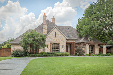Large traditional beige one-story stone house exterior idea in Dallas with a hip roof and a shingle roof