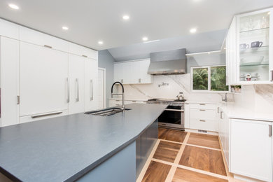 Example of a mid-sized trendy medium tone wood floor and multicolored floor eat-in kitchen design in Vancouver with an integrated sink, shaker cabinets, white cabinets, quartz countertops, white backsplash, quartz backsplash, stainless steel appliances, an island and gray countertops