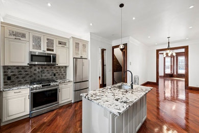 Inspiration for a mid-sized transitional single-wall medium tone wood floor and brown floor open concept kitchen remodel in New York with an undermount sink, beaded inset cabinets, beige cabinets, granite countertops, multicolored backsplash, stainless steel appliances, an island and multicolored countertops