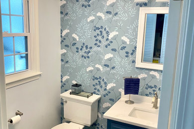 Bathroom - small transitional porcelain tile, gray floor, single-sink and wallpaper bathroom idea in Boston with raised-panel cabinets, blue cabinets, a two-piece toilet, blue walls, an undermount sink, quartz countertops, white countertops and a built-in vanity