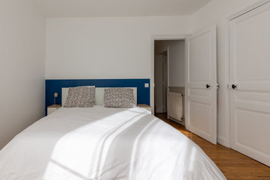 Cette image montre une chambre parentale minimaliste de taille moyenne avec un mur blanc, parquet clair et dressing.
