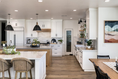 Inspiration for a large cottage vinyl floor and brown floor kitchen remodel in Other with a farmhouse sink, shaker cabinets, white cabinets, quartzite countertops, white backsplash, subway tile backsplash, stainless steel appliances, two islands and white countertops
