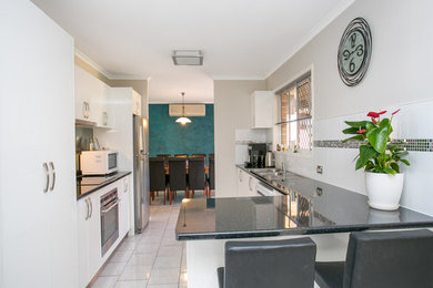 Photo of a mid-sized modern galley eat-in kitchen in Sunshine Coast with a double-bowl sink, flat-panel cabinets, white cabinets, laminate benchtops, white splashback, ceramic splashback, stainless steel appliances, ceramic floors and no island.