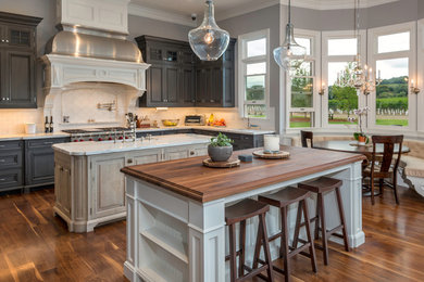 This is an example of a large traditional u-shaped eat-in kitchen in San Francisco with a farmhouse sink, recessed-panel cabinets, grey cabinets, marble benchtops, white splashback, subway tile splashback, stainless steel appliances, medium hardwood floors and multiple islands.