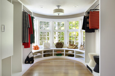 Example of a large minimalist light wood floor walk-in closet design in New York with white cabinets