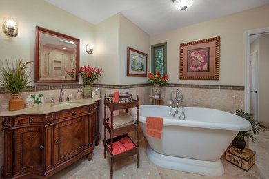 Bathroom - mid-sized mediterranean master beige tile and stone tile terrazzo floor and beige floor bathroom idea in Raleigh with furniture-like cabinets, brown cabinets, a one-piece toilet, beige walls, an undermount sink, marble countertops, a hinged shower door and beige countertops