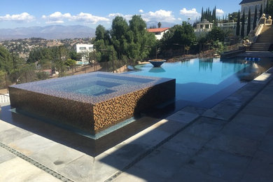 This is an example of a large contemporary backyard custom-shaped infinity pool in Los Angeles with a hot tub and stamped concrete.