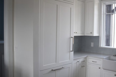 Small farmhouse u-shaped dark wood floor and brown floor eat-in kitchen photo in Other with a farmhouse sink, flat-panel cabinets, white cabinets, quartzite countertops, gray backsplash, porcelain backsplash, paneled appliances and an island