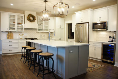 Eat-in kitchen - large country l-shaped dark wood floor and brown floor eat-in kitchen idea in Detroit with a farmhouse sink, shaker cabinets, white cabinets, white backsplash, subway tile backsplash, stainless steel appliances, an island and white countertops