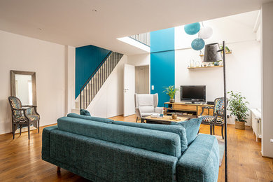 Cette image montre une salle de séjour bohème ouverte avec un mur bleu, parquet clair, un téléviseur indépendant et un sol beige.