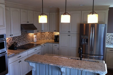 Eat-in kitchen - mid-sized traditional u-shaped medium tone wood floor eat-in kitchen idea in Other with an undermount sink, raised-panel cabinets, white cabinets, granite countertops, multicolored backsplash, glass tile backsplash, stainless steel appliances and an island