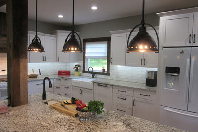 Eat-in kitchen - country l-shaped dark wood floor eat-in kitchen idea in Other with a farmhouse sink, shaker cabinets, white cabinets, granite countertops, white backsplash, porcelain backsplash, white appliances and an island