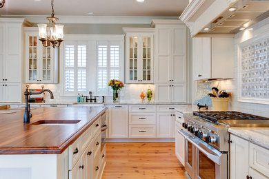 Example of a large transitional l-shaped medium tone wood floor kitchen design in Charleston with a farmhouse sink, white cabinets, white backsplash, subway tile backsplash, stainless steel appliances, an island, recessed-panel cabinets and granite countertops