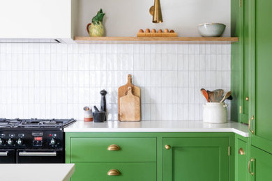 Photo of a mid-sized modern l-shaped eat-in kitchen in Other with a farmhouse sink, shaker cabinets, green cabinets, quartzite benchtops, white splashback, ceramic splashback, black appliances, porcelain floors, with island, multi-coloured floor and white benchtop.