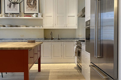 This is an example of a large eclectic grey and white l-shaped kitchen/diner in London with a double-bowl sink, shaker cabinets, white cabinets, marble worktops, white splashback, marble splashback, stainless steel appliances, light hardwood flooring, an island, white floors, white worktops, a drop ceiling and feature lighting.
