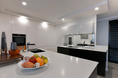 Photo of a large modern eat-in kitchen in Newcastle - Maitland with an undermount sink, flat-panel cabinets, black cabinets, laminate benchtops, metallic splashback, mirror splashback, black appliances, ceramic floors, with island, beige floor and white benchtop.