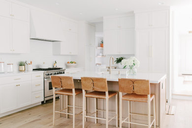 Example of a mid-sized beach style l-shaped light wood floor and beige floor eat-in kitchen design in San Diego with a farmhouse sink, shaker cabinets, light wood cabinets, quartz countertops, white backsplash, ceramic backsplash, paneled appliances, an island and white countertops