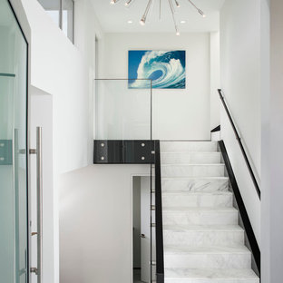This is an example of a large beach style straight glass railing staircase in San Diego with marble treads and marble risers.