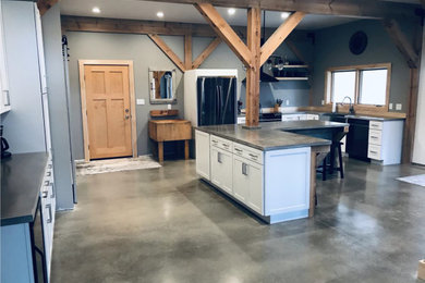 Example of a large farmhouse l-shaped concrete floor, gray floor and exposed beam eat-in kitchen design in Chicago with a farmhouse sink, shaker cabinets, white cabinets, concrete countertops, black appliances, an island and gray countertops