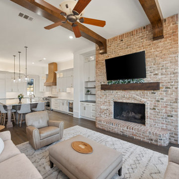 Open-concept living and kitchen area with brick accent wall and wood beams