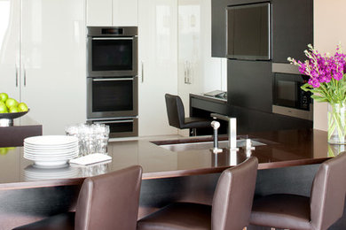 Inspiration for a contemporary u-shaped light wood floor eat-in kitchen remodel in New York with flat-panel cabinets, an undermount sink, dark wood cabinets, white backsplash, glass sheet backsplash, stainless steel appliances and no island