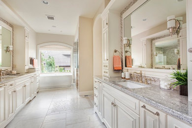 Example of a large classic master beige tile porcelain tile, white floor and double-sink freestanding bathtub design in Dallas with raised-panel cabinets, white cabinets, beige walls, an undermount sink, granite countertops, gray countertops and a built-in vanity