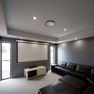 Example of a large trendy enclosed carpeted home theater design in Brisbane with gray walls and a projector screen