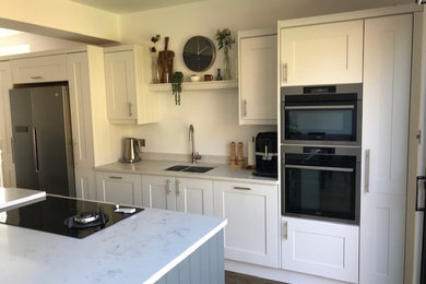 This is an example of a medium sized contemporary grey and white single-wall kitchen in Manchester with shaker cabinets, stainless steel appliances, vinyl flooring, an island and white worktops.