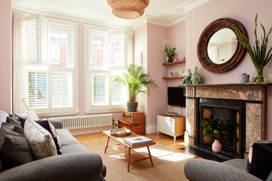 Medium sized classic formal and grey and pink enclosed living room in London with pink walls, light hardwood flooring, a standard fireplace, a stone fireplace surround, a freestanding tv and feature lighting.
