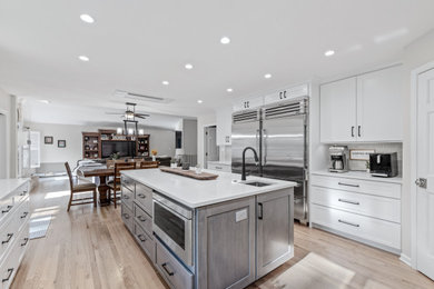 Inspiration for a large transitional u-shaped light wood floor and multicolored floor eat-in kitchen remodel in Other with a single-bowl sink, shaker cabinets, white cabinets, quartz countertops, white backsplash, quartz backsplash, stainless steel appliances, an island and white countertops